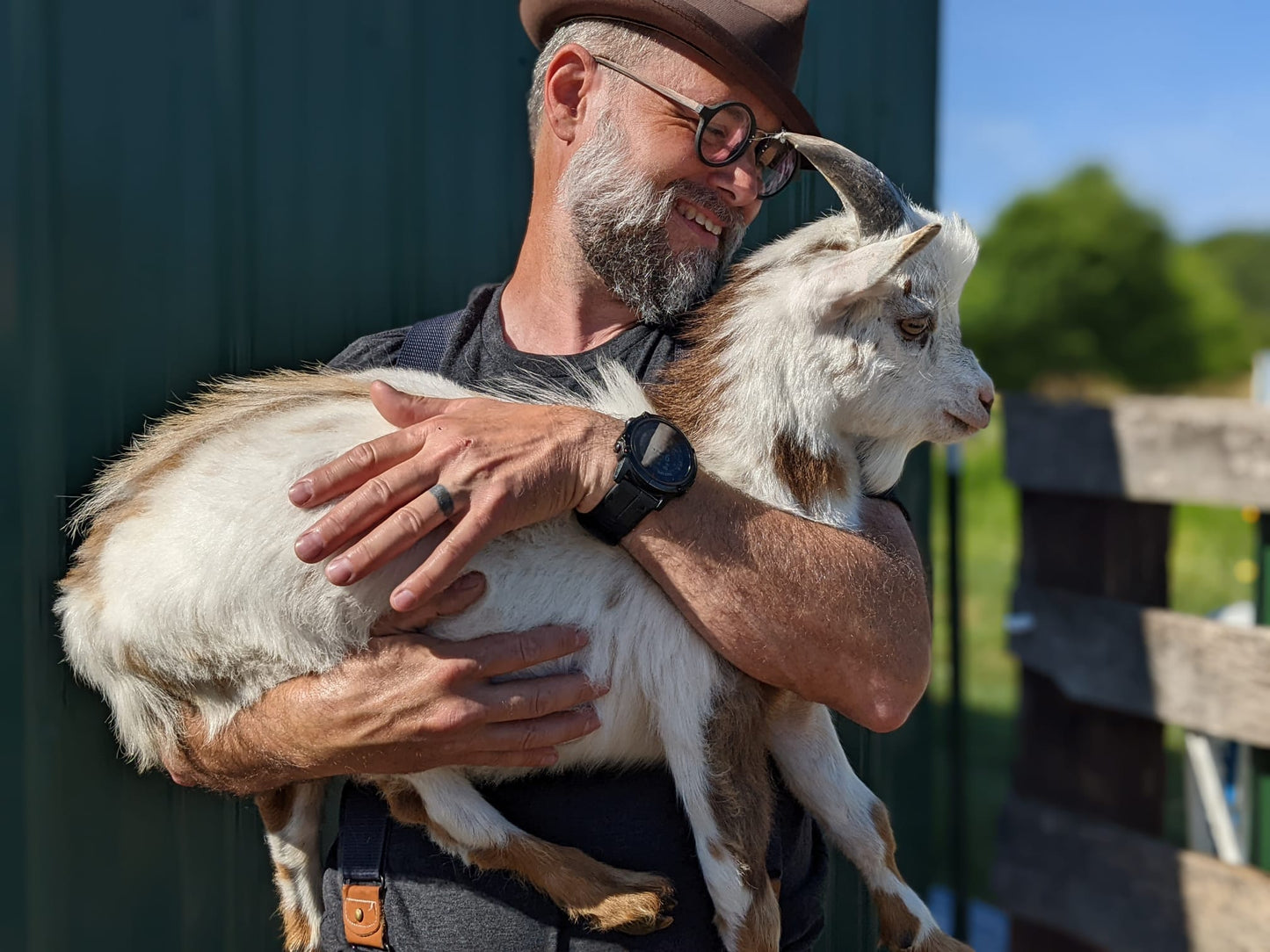 Smiling man in a hat holding a goat